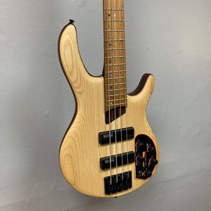 Cort Artisan B4 Element Natural, a wooden electric guitar with Bartolini MK-1 pickups and a MetalCraft M4 bridge, displayed on a wall.