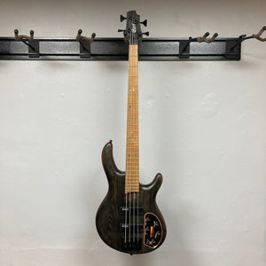 Cort Artisan B4 Element bass guitar on a wall hook, showcasing its 5-piece walnut/panga-panga neck and roasted maple fretboard.