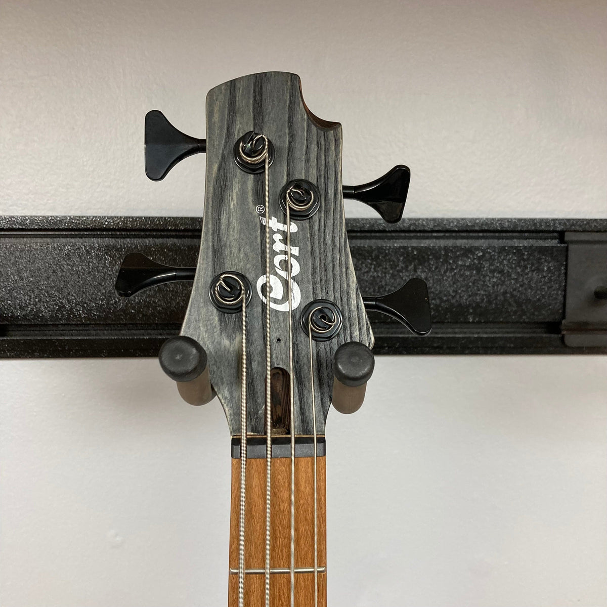 Close-up of the Cort Artisan B4 Element Open Pore Black guitar headstock, showcasing tuning pegs and part of the neck.
