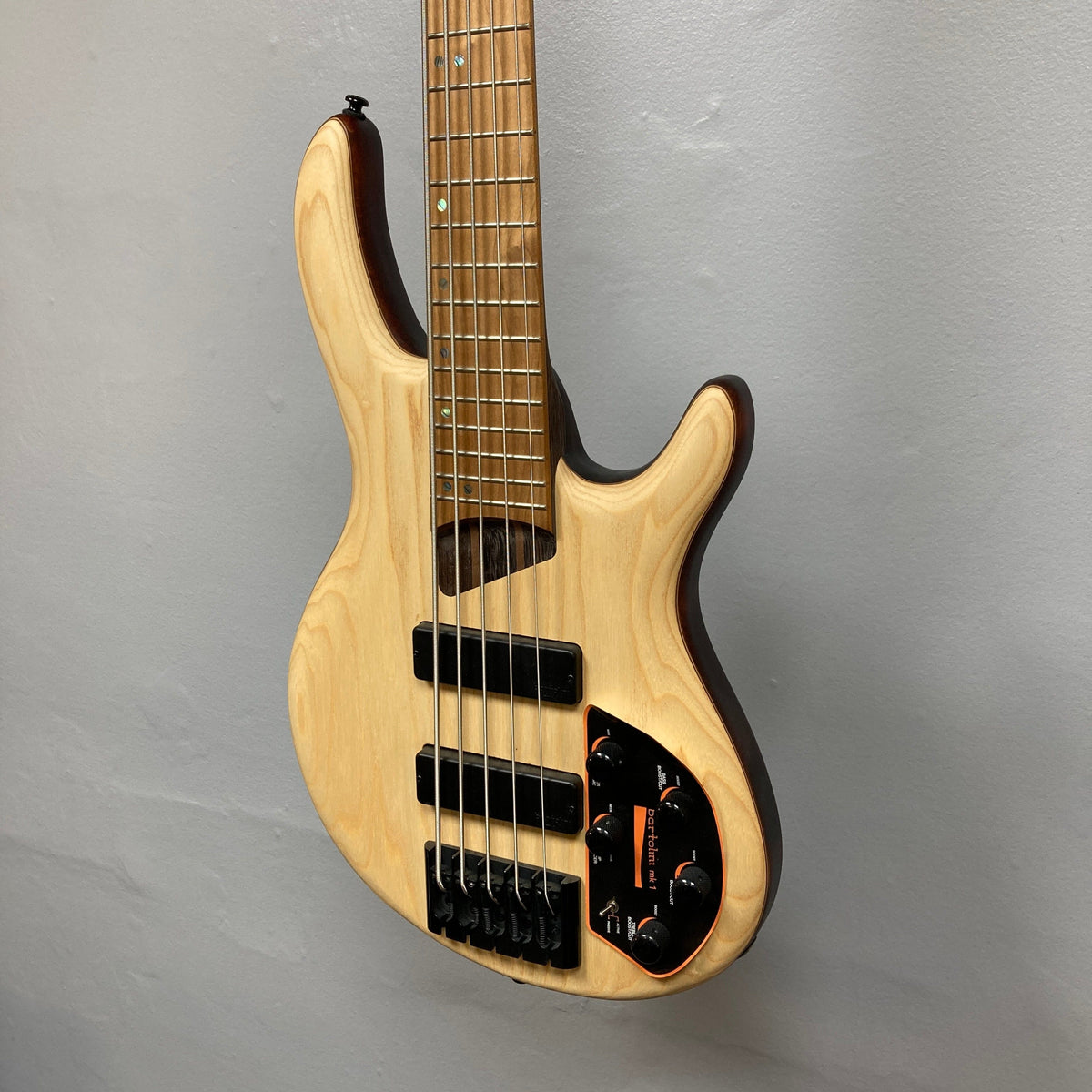 Cort Artisan B5 Element Natural Used, a wooden electric guitar, showcasing its ergonomic mahogany body and advanced features, mounted on a wall.