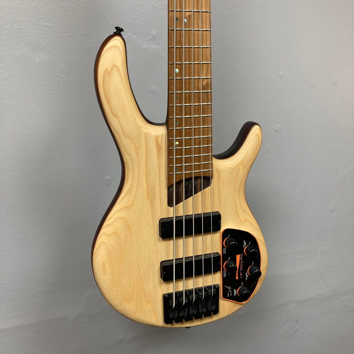 Cort Artisan B5 Element Natural Used bass guitar on wall, highlighting its roasted maple fretboard and ergonomic body, with visible Bartolini pickups and MetalCraft M5 bridges.