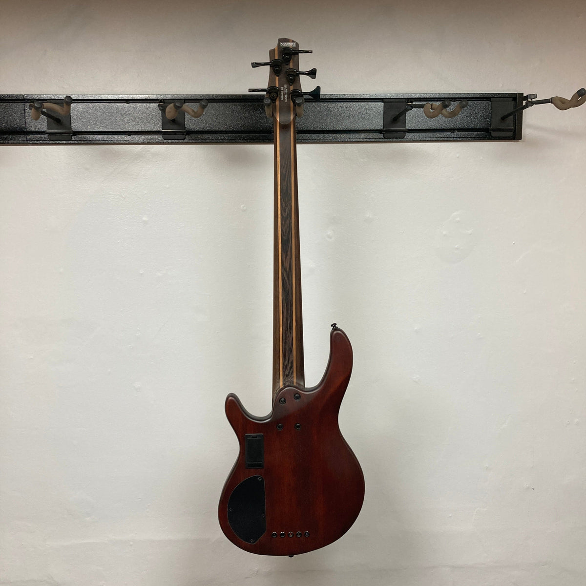 Cort Artisan B5 Element bass guitar on wall, showcasing Hipshot® tuners, roasted maple fretboard, and MetalCraft M5 bridges for enhanced tone.