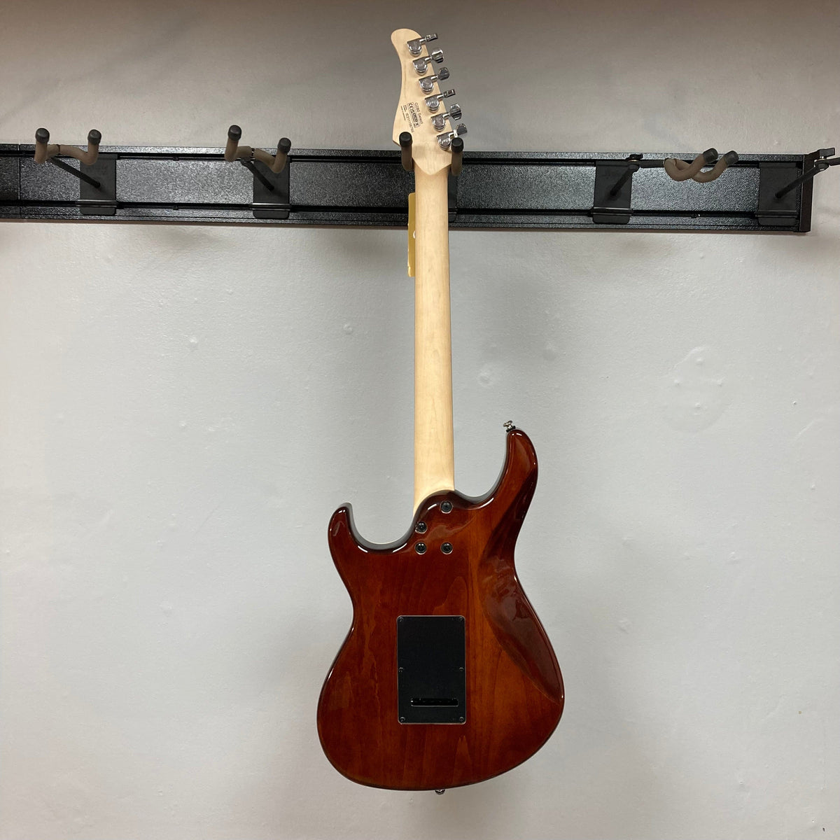 Cort G280 Select Amber electric guitar on a wall hook, showcasing its Pearloid pickguard, Rosewood fingerboard, and high-grade Voiced Tone VTH-77 humbucker.