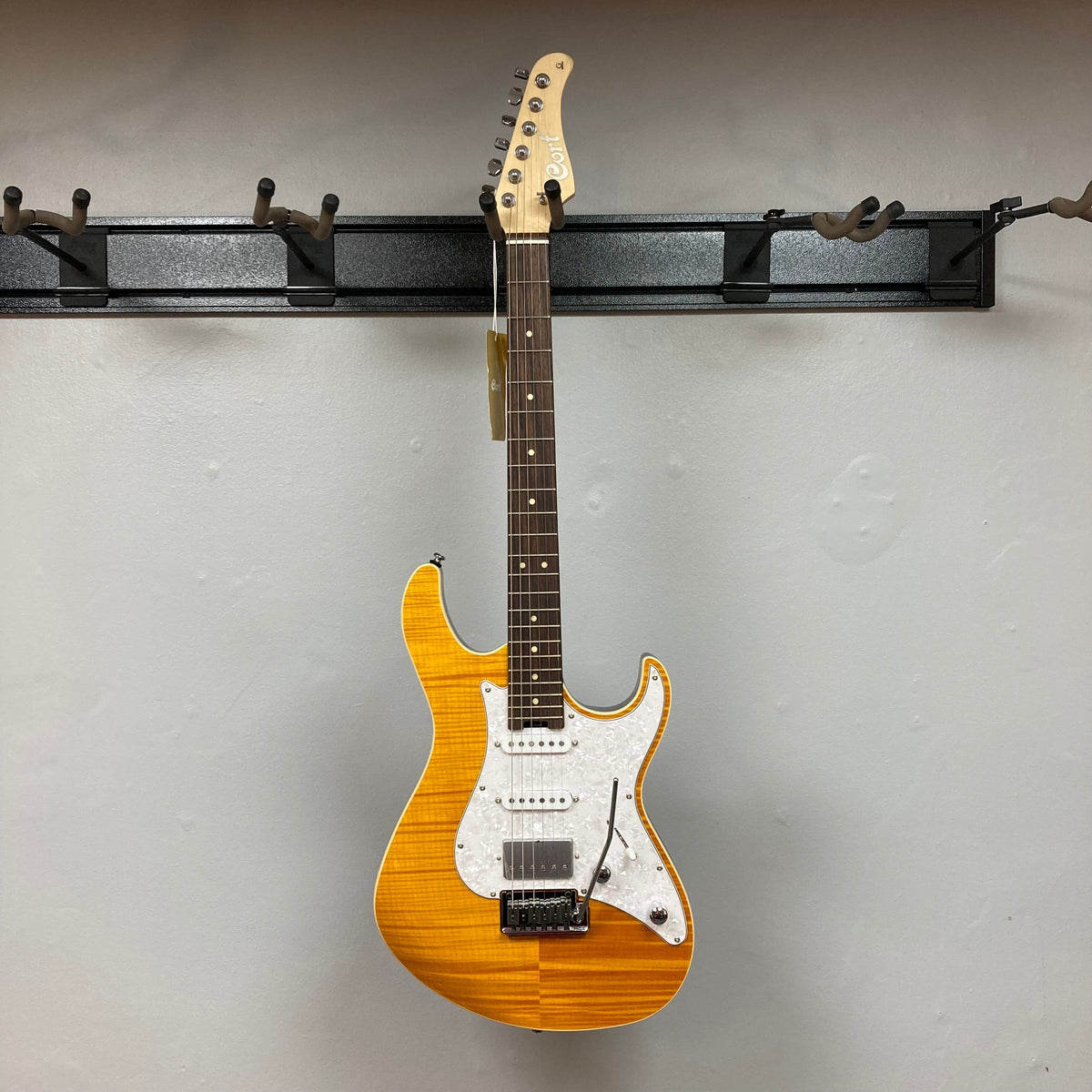 Cort G280 Select Amber electric guitar with Rosewood fretboard, Pearloid pickguard, and humbucker pickups, displayed on a wall.