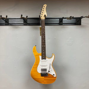 Cort G280 Select Amber electric guitar with Rosewood fretboard, Pearloid pickguard, and humbucker pickups, displayed on a wall.