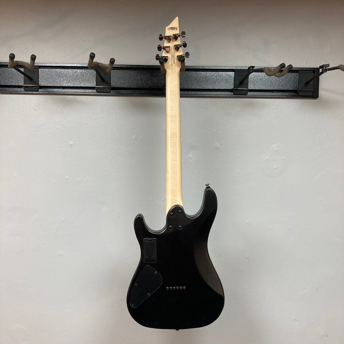 Cort KX300 EBR Etched Black Red electric guitar with a matte black finish, red and gold accents, mounted on a wall.