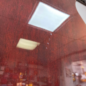 Close-up of a polished, reddish-brown Crafter SA-BUB Acoustic Electric Guitar Used Consign reflecting ceiling lights. Minor dings are visible on the finish, and the blurred background highlights its plugged-in performance. Brand: Crafter.