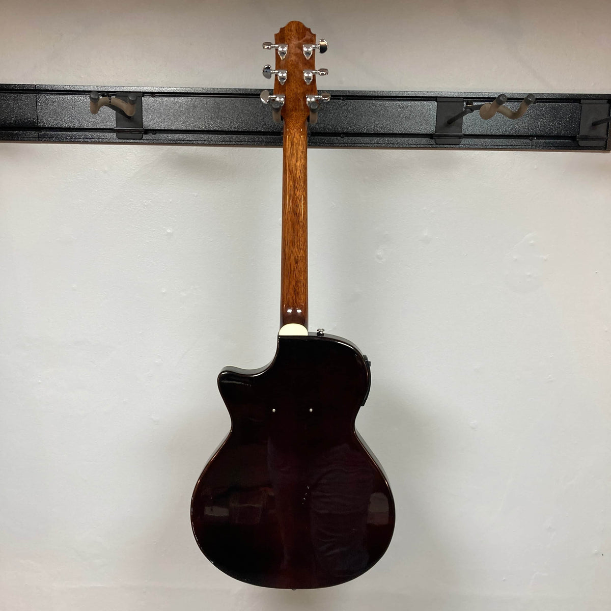 A Crafter SA-BUB Acoustic Electric Guitar Used Consign by Crafter hangs on a wall mount, displaying its wooden neck and tuning pegs. The dark brown back contrasts against a plain white wall—ideal for both acoustic and electric performances.
