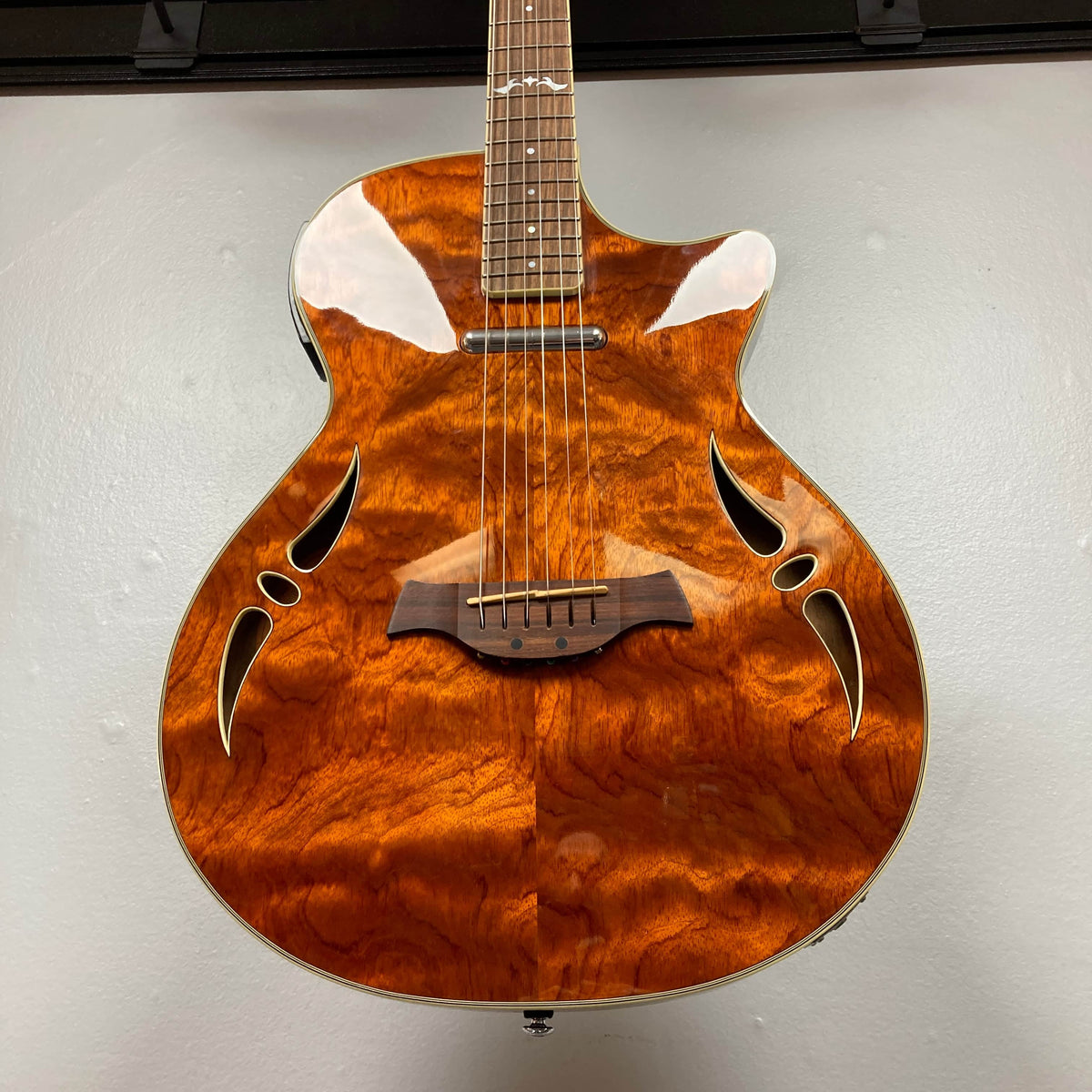A close-up of a Crafter SA-BUB Acoustic Electric Guitar Used Consign by Crafter, featuring a polished figured wood top, f-hole style sound holes, and wooden bridge, ideal for plugged-in performances against a plain white background.