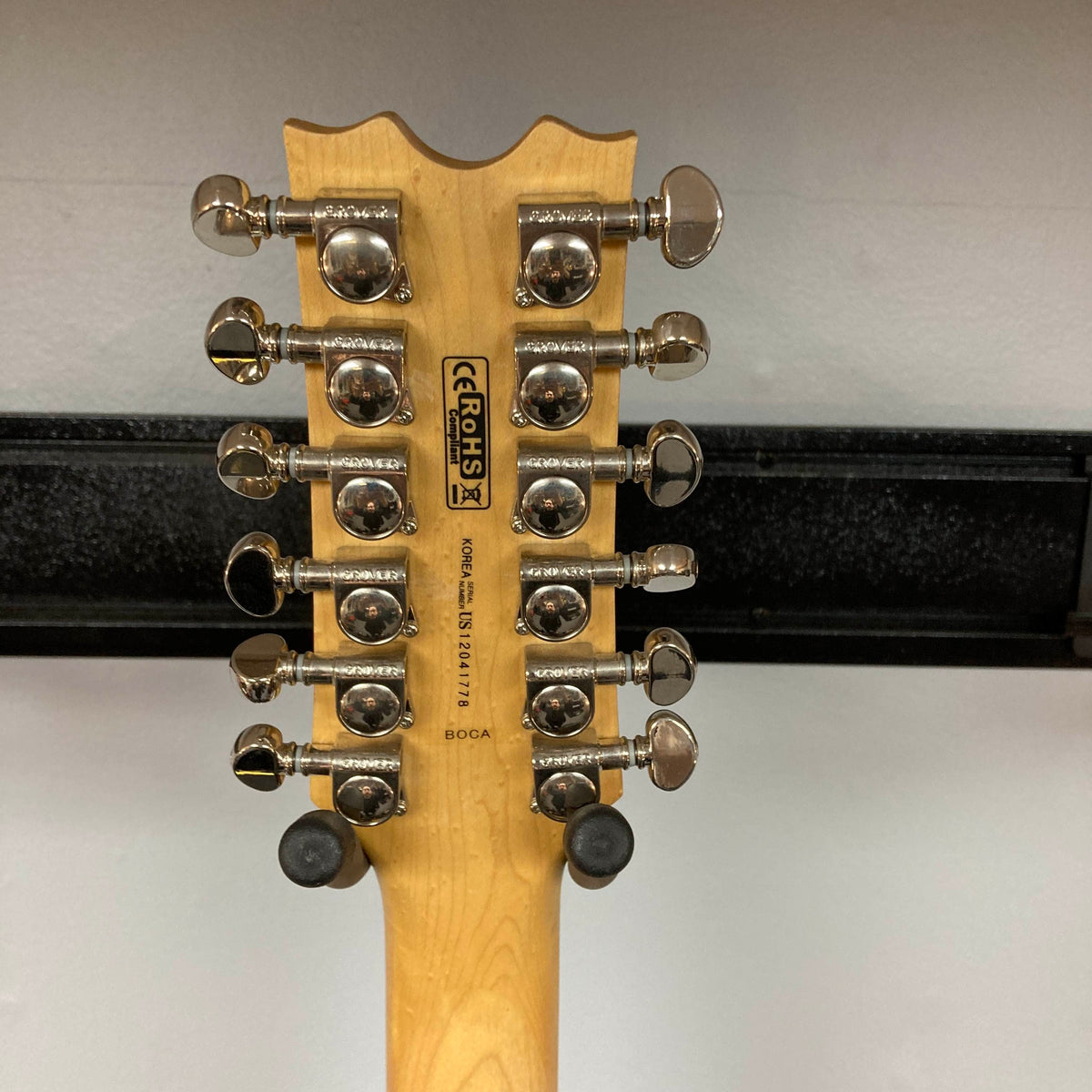 The back of a Dean Boca Trans Amber Burst 12 String w/Gigbag headstock by Dean shows twelve upward-facing tuning pegs and a serial number against a plain background.
