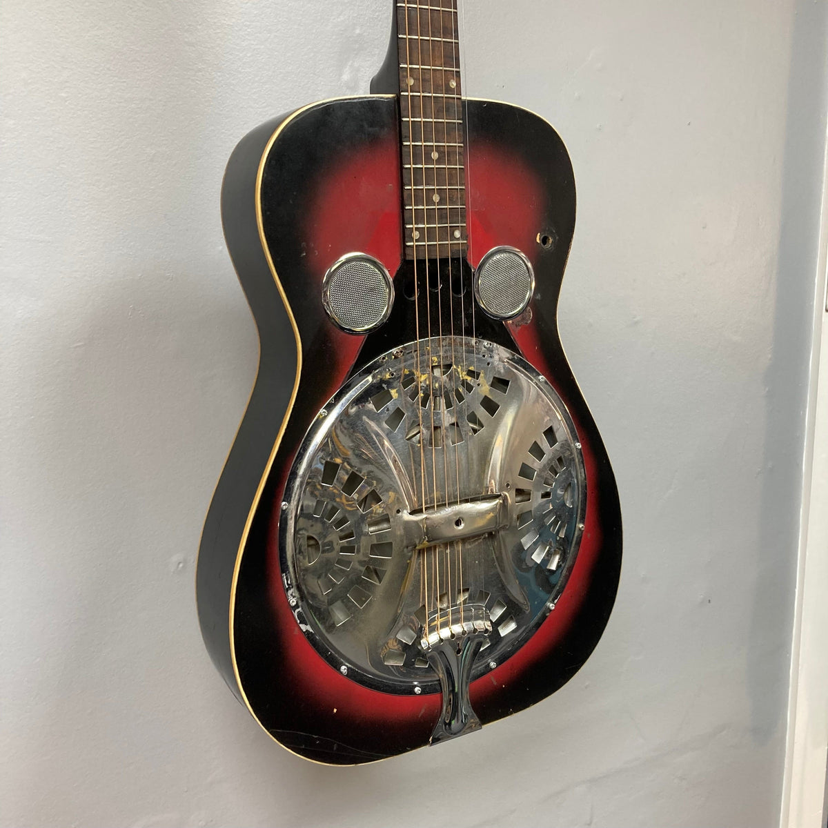 Dobro Model 60 DS Round Neck 1970s Red Burst resonator guitar with metal cover and visible strings, showing wear from use.