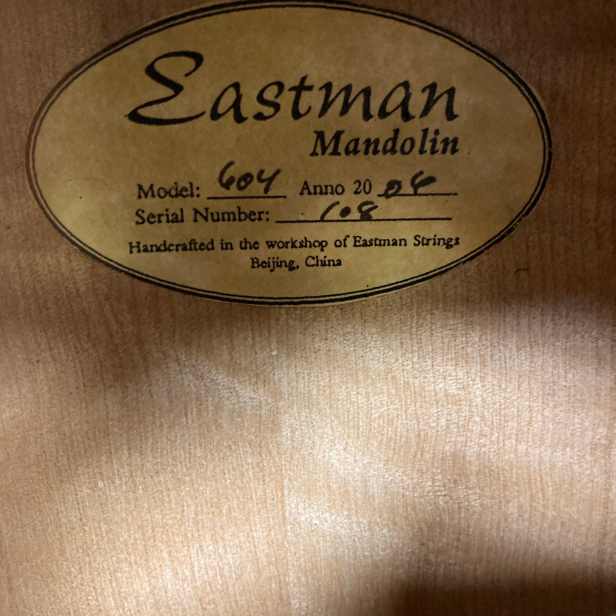 Eastman MD604-GB A-Style Oval-Hole Mandolin on wood surface, showcasing detailed label. Ideal for musicians; includes case. Consignment item at Guitars on Main.
