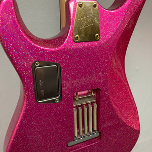A close-up of the back of the Edwards ESP E-SN-185-TO Takayoshi Ohmura Twinkle Pink electric guitar by Edwards, highlighting its metallic hardware, tremolo spring cavity, and control plate.