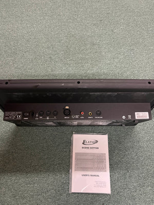 Back panel of the Elation Scene Setter 24-Channel DMX Dimmer Console by Elation, displaying multiple input/output ports, shown above its user manual on a carpeted floor—ideal for professional lighting control and scene programming.