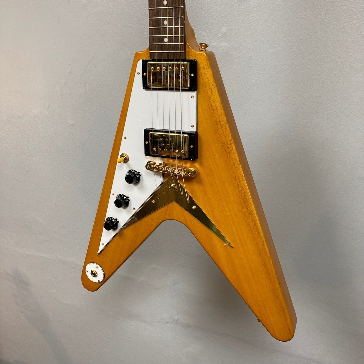 Epiphone 1958 Korina Flying V Left handed w/Case, showcasing its triangle body and intricate craftsmanship, mounted on a wall.