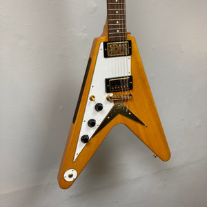 Epiphone 1958 Korina Flying V Left handed guitar on a wall, showcasing its solid body, long neck tenon, and detailed hardware.