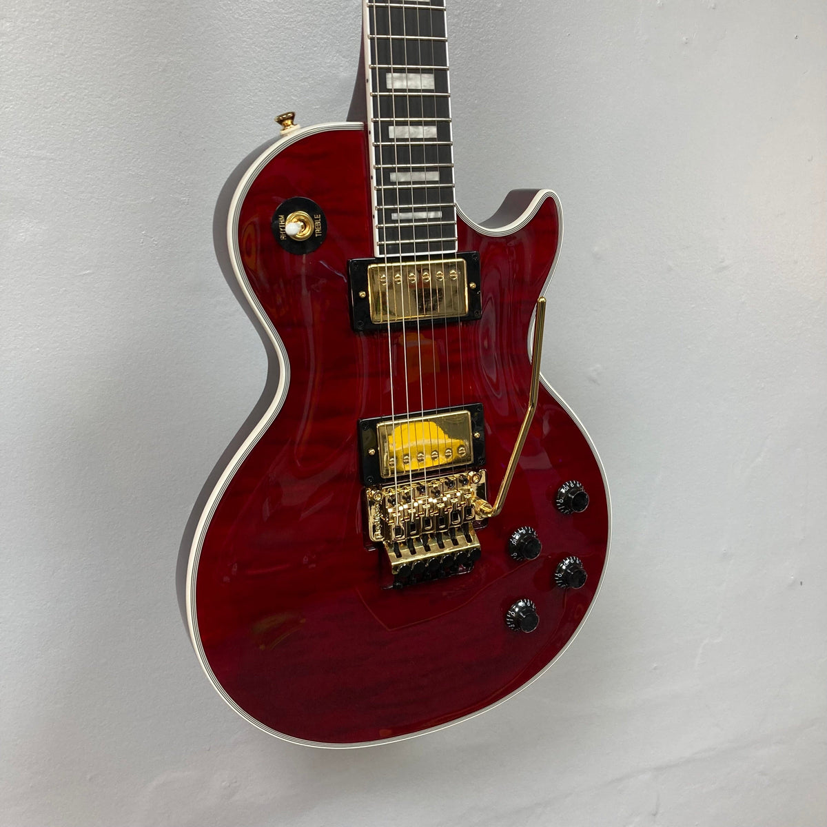 Epiphone Alex Lifeson Les Paul Custom Axcess guitar with gold hardware, displayed on a wall.