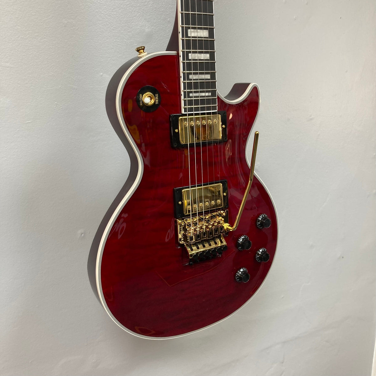 Epiphone Alex Lifeson Les Paul Custom Axcess w/Case, featuring gold hardware and Floyd Rose tremolo, displayed against a wall.