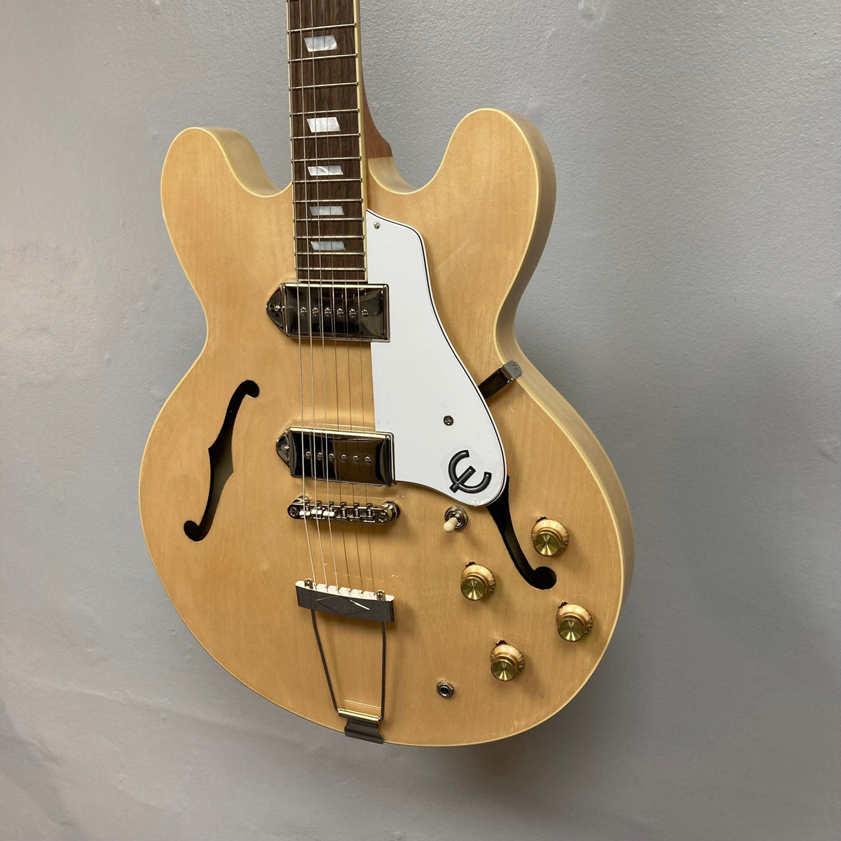 Epiphone Casino Natural guitar, close-up of strings, gold dial, and vintage lock, showcasing its hollowbody design and detailed craftsmanship.