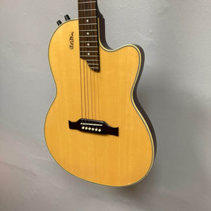 An Epiphone Chet Atkins SST Studio Natural acoustic-electric guitar, made in Korea, is displayed on a light gray wall. It features six tuning pegs, control knobs, a cutaway body, and comes with a hard case.