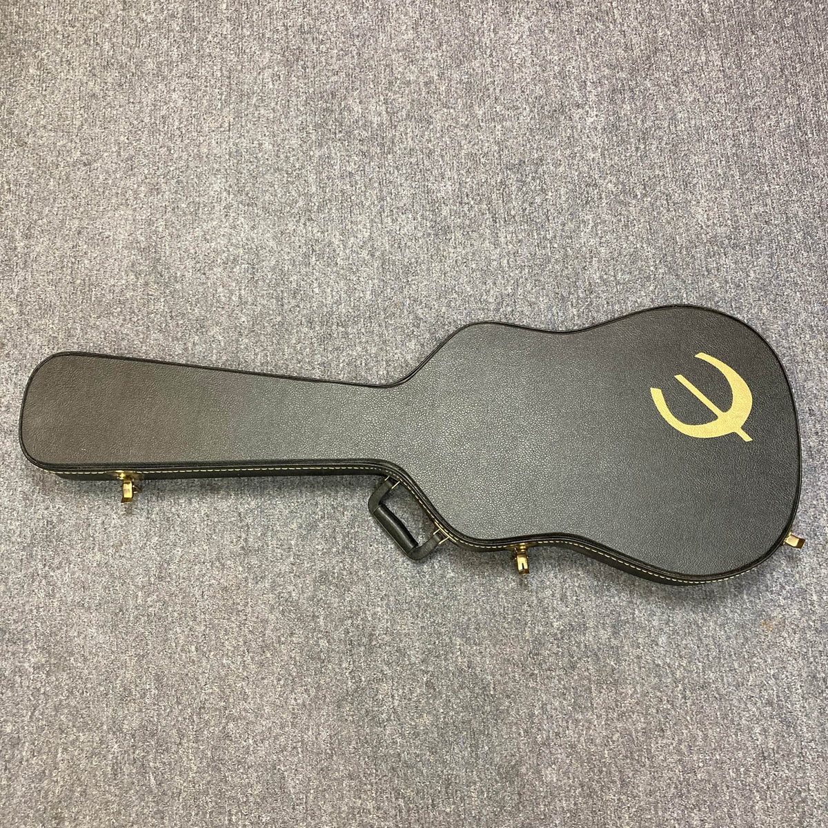 A black Epiphone hard case with gold logo and latches, designed for the Chet Atkins SST Studio Natural Korea acoustic-electric guitar, lies closed on a gray carpeted floor; it includes a handle for easy carrying.