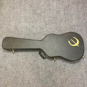A black Epiphone hard case with gold logo and latches, designed for the Chet Atkins SST Studio Natural Korea acoustic-electric guitar, lies closed on a gray carpeted floor; it includes a handle for easy carrying.