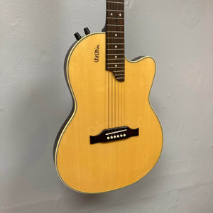 A close-up of an Epiphone Chet Atkins SST Studio Natural acoustic-electric guitar, made in Korea, with a light wood top and cutaway body, mounted on a light gray wall. Includes hard case; used consignment.