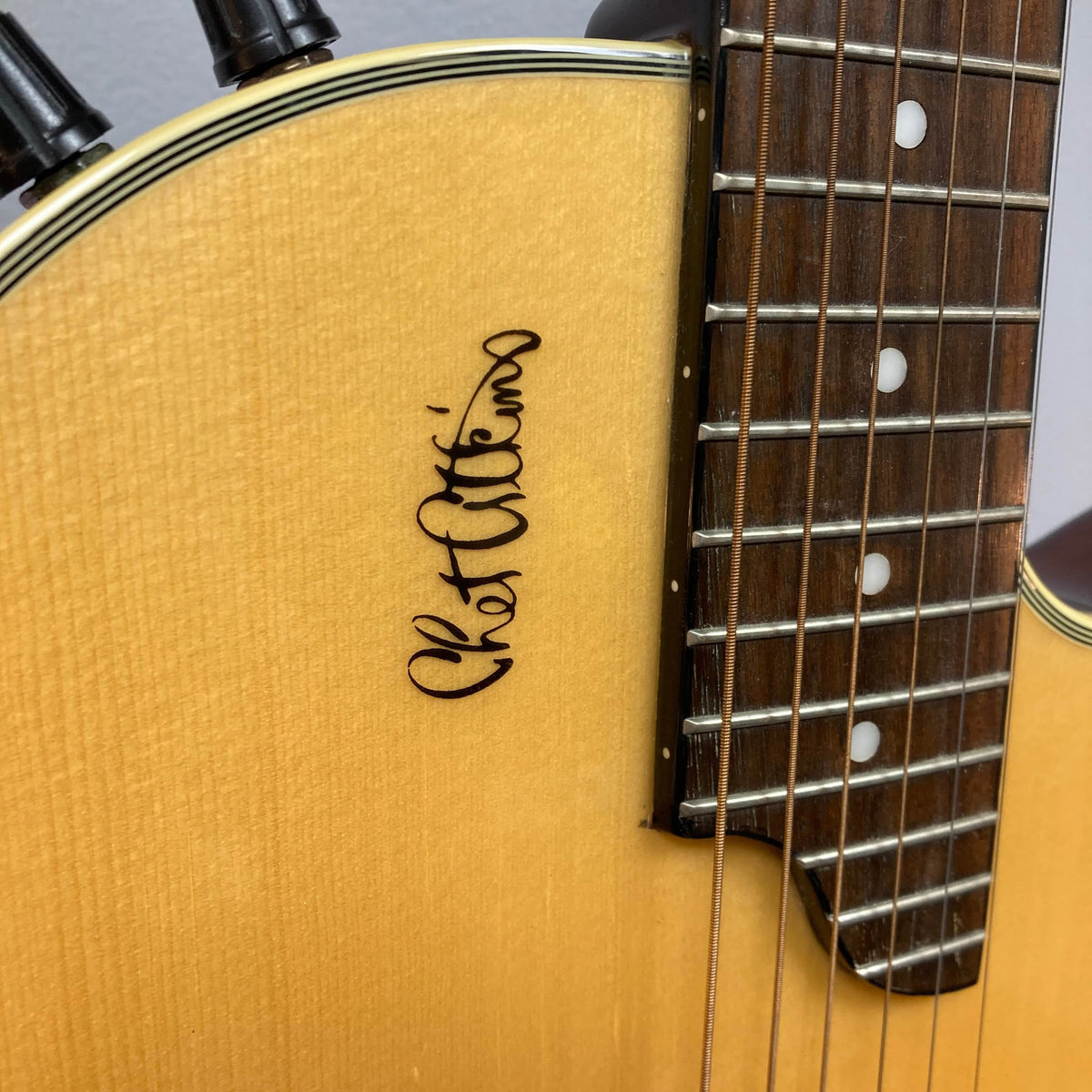 Close-up of an Epiphone Chet Atkins SST Studio Natural (Korea) guitar body by Epiphone, showing part of the fretboard and "Chet Atkins" signature on the light wood finish, highlighting its feedback-resistant acoustic-electric design.