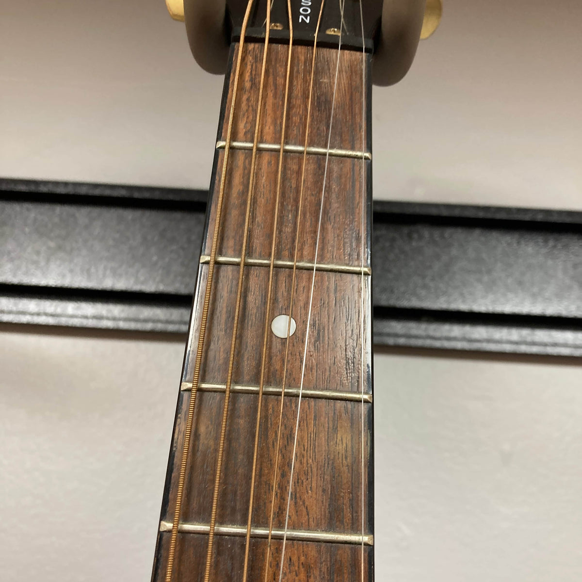 Close-up of the Epiphone Chet Atkins SST Studio Natural Korea guitar neck, featuring six strings, metal frets, a circular fifth-fret inlay, and wooden fingerboard; its feedback-resistant acoustic-electric design appears in the background.