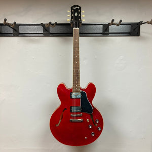 Epiphone ES-335 semi-hollowbody electric guitar on a wall hook, featuring knobs and a classic design.