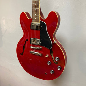 Epiphone ES-335 Semi-hollowbody Electric Guitar - Cherry, featuring knobs, strings, and dials, mounted on a wall.