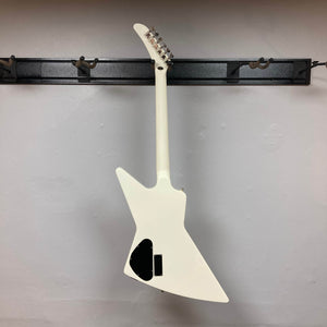 An Epiphone Explorer 80s EMG Classic White with a mahogany neck hangs backward on a wall-mounted rack, displaying its back and headstock.