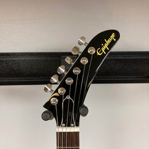 Close-up of the headstock of the Epiphone Explorer 80s EMG Classic White guitar by Epiphone, showing six tuning pegs against a light wall and a horizontal black metal bar.