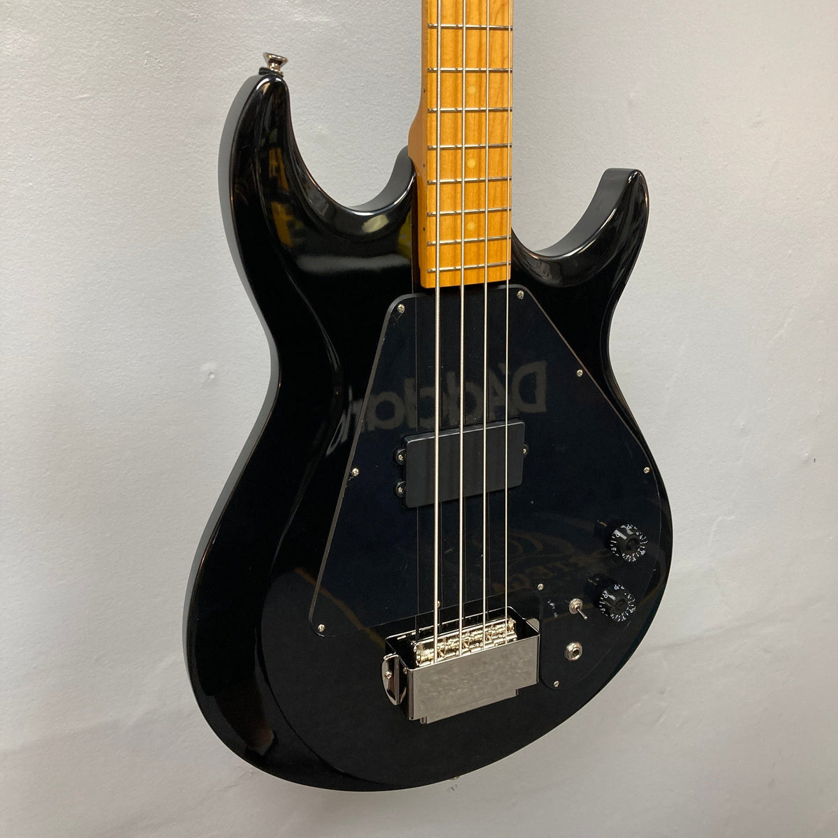 Epiphone Grabber Bass Ebony displayed on wall, showcasing its sleek design and maple neck, ideal for versatile tones and modern playability.