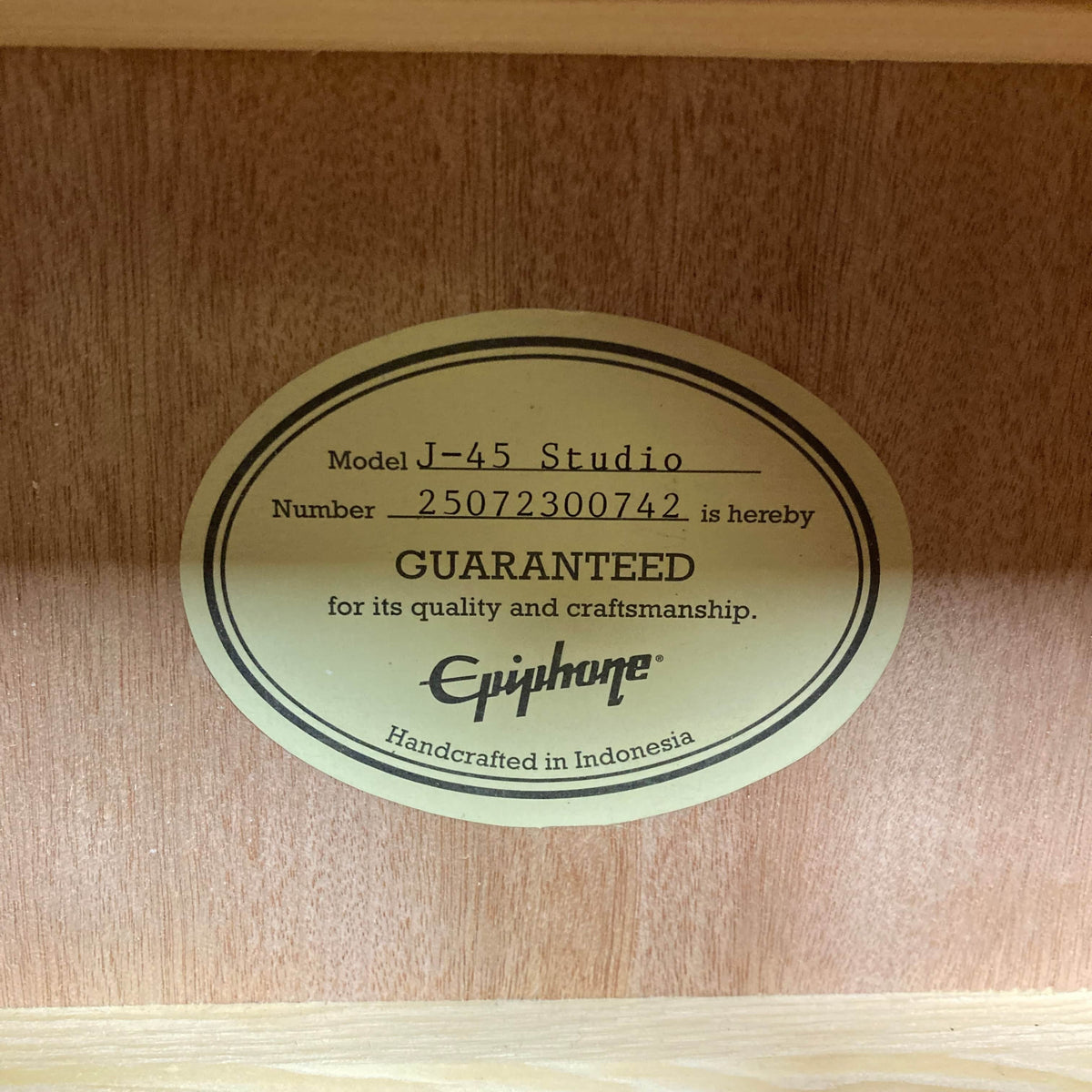 Inside the Epiphone J-45 Studio Vintage Sunburst w/Gigbag, an oval label reads: "Model J-45 Studio, Number 25072300742 is hereby GUARANTEED for its quality and craftsmanship. Epiphone. Handcrafted in Indonesia.