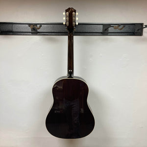 An Epiphone J-45 Studio Vintage Sunburst acoustic guitar hangs on a wall rack, its glossy dark wood finish, light binding, and solid spruce top standing out against the plain white wall. Includes Gigbag.