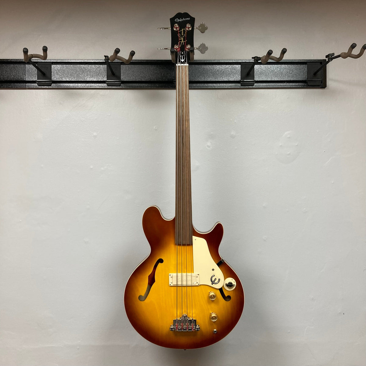 Epiphone Jack Casady Fretless Bass - Aged Royal Tan displayed on a wall, showcasing its archtop body and nickel finish.
