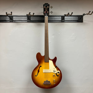 Epiphone Jack Casady Fretless Bass - Aged Royal Tan displayed on a wall, showcasing its archtop body and nickel finish.