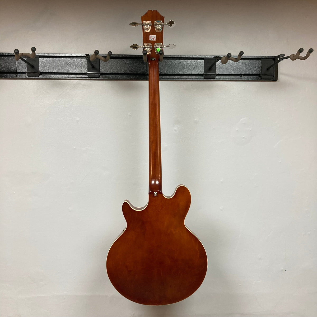 Epiphone Jack Casady Fretless Bass - Aged Royal Tan displayed on a wall, highlighting its archtop body and layered maple construction.