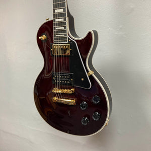 An Epiphone Jerry Cantrell Wino Les Paul Custom in Wine Red with gold hardware and black pickguard hangs on a light gray wall; when not displayed, its custom hardshell case by Epiphone keeps it safe.