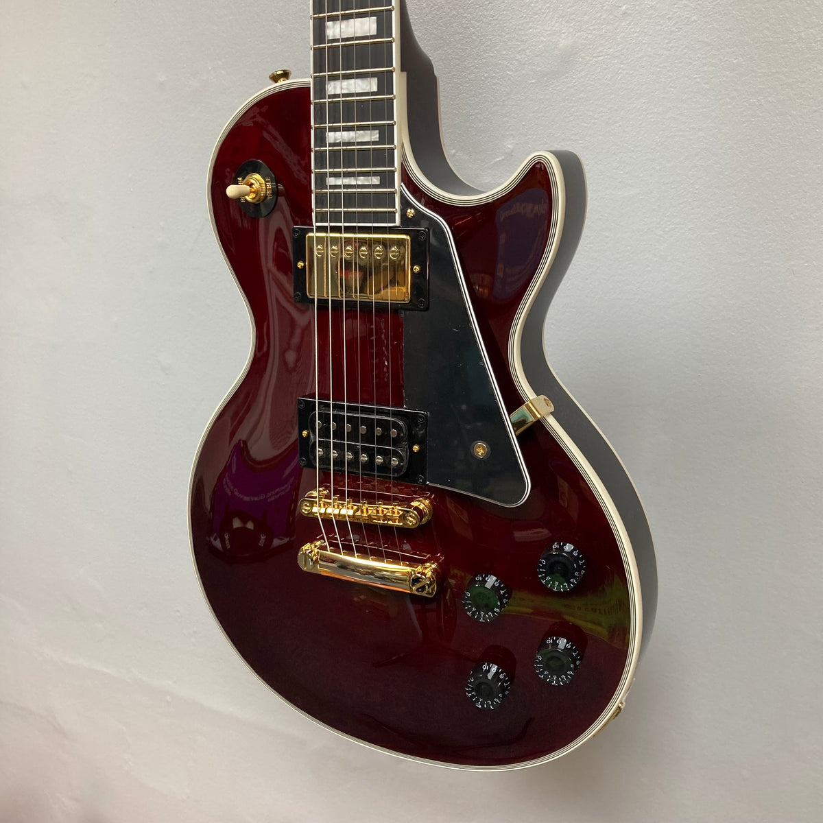 Epiphone Jerry Cantrell Wino Les Paul Custom Wine Red guitar displayed on a wall, featuring gold hardware and custom details.