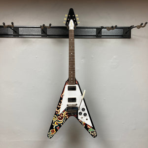 Epiphone Jimi Hendrix Love Drops Flying V guitar, on a wall hook, showcasing its iconic psychedelic design. Includes a hard case for protection.