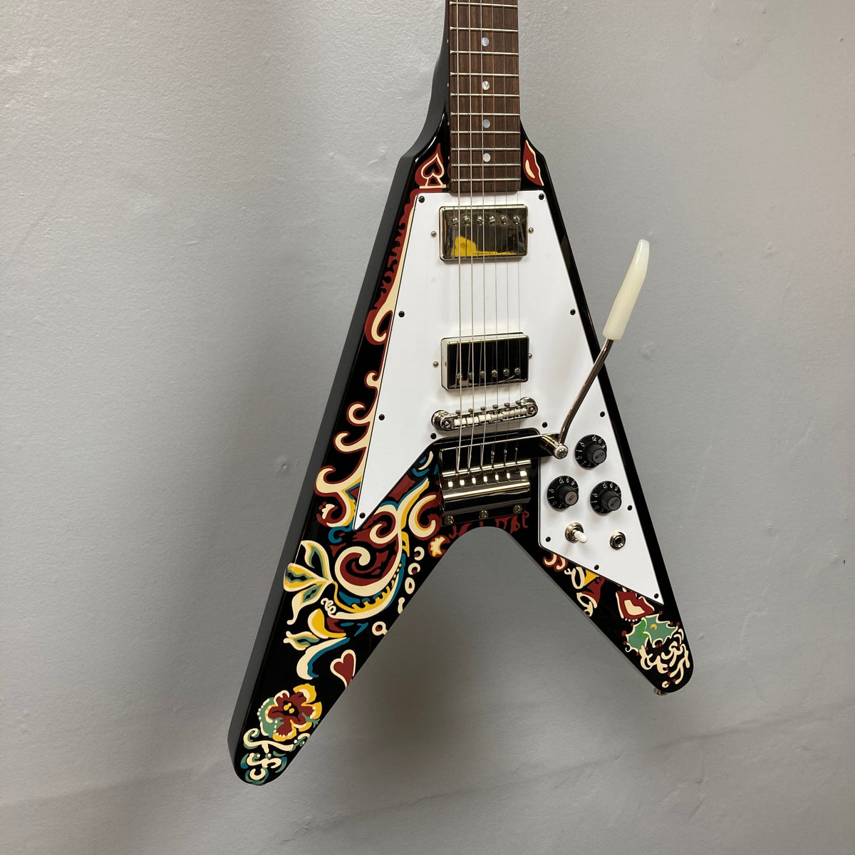 Epiphone Jimi Hendrix Love Drops Flying V guitar displayed on a wall, showcasing its distinctive psychedelic design and craftsmanship, with hard case included.
