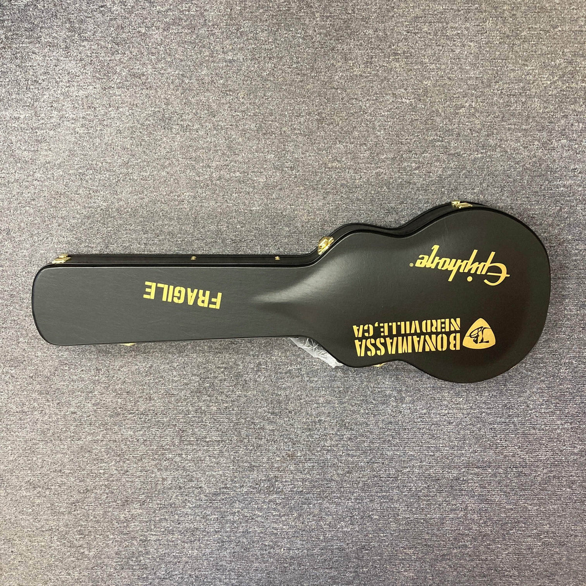 Epiphone Joe Bonamassa 59 Les Paul Custom Bigsby guitar case, black with gold hardware, featuring FRAGILE stencil and custom decal, on gray carpet.