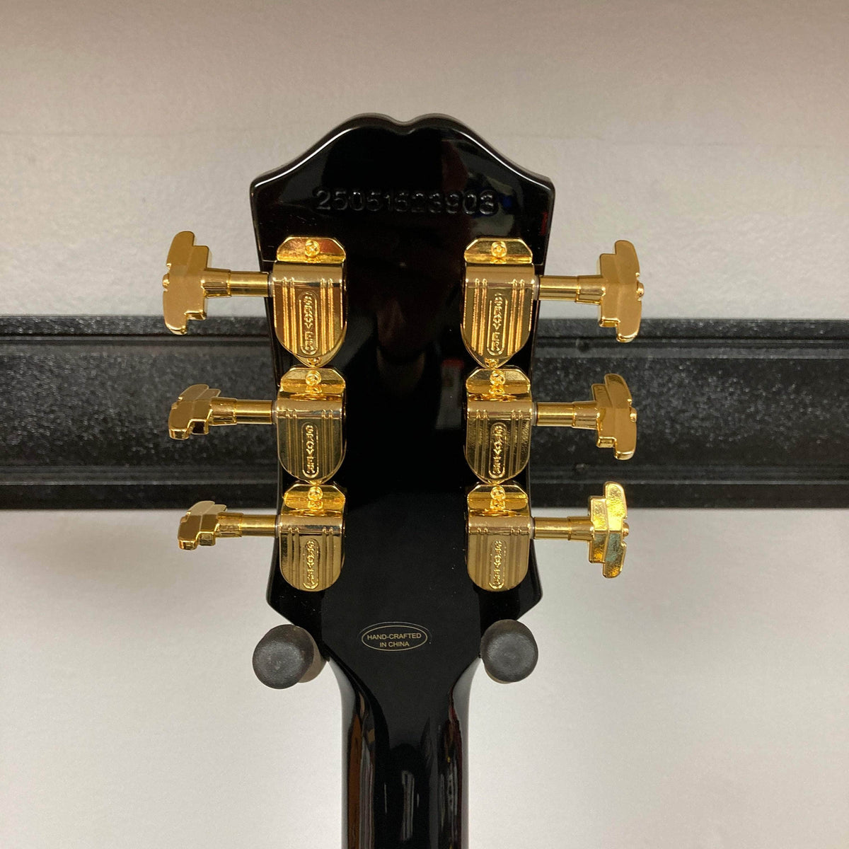 Back view of Epiphone Joe Bonamassa 59 Les Paul Custom Bigsby, featuring gold tuners and Hand-crafted in China badge, mounted on a wall hanger.
