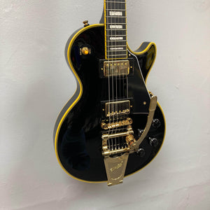 Epiphone Joe Bonamassa '59 Les Paul Custom with Bigsby, featuring gold hardware, dual humbuckers, and block inlays, showcased against a light wall.