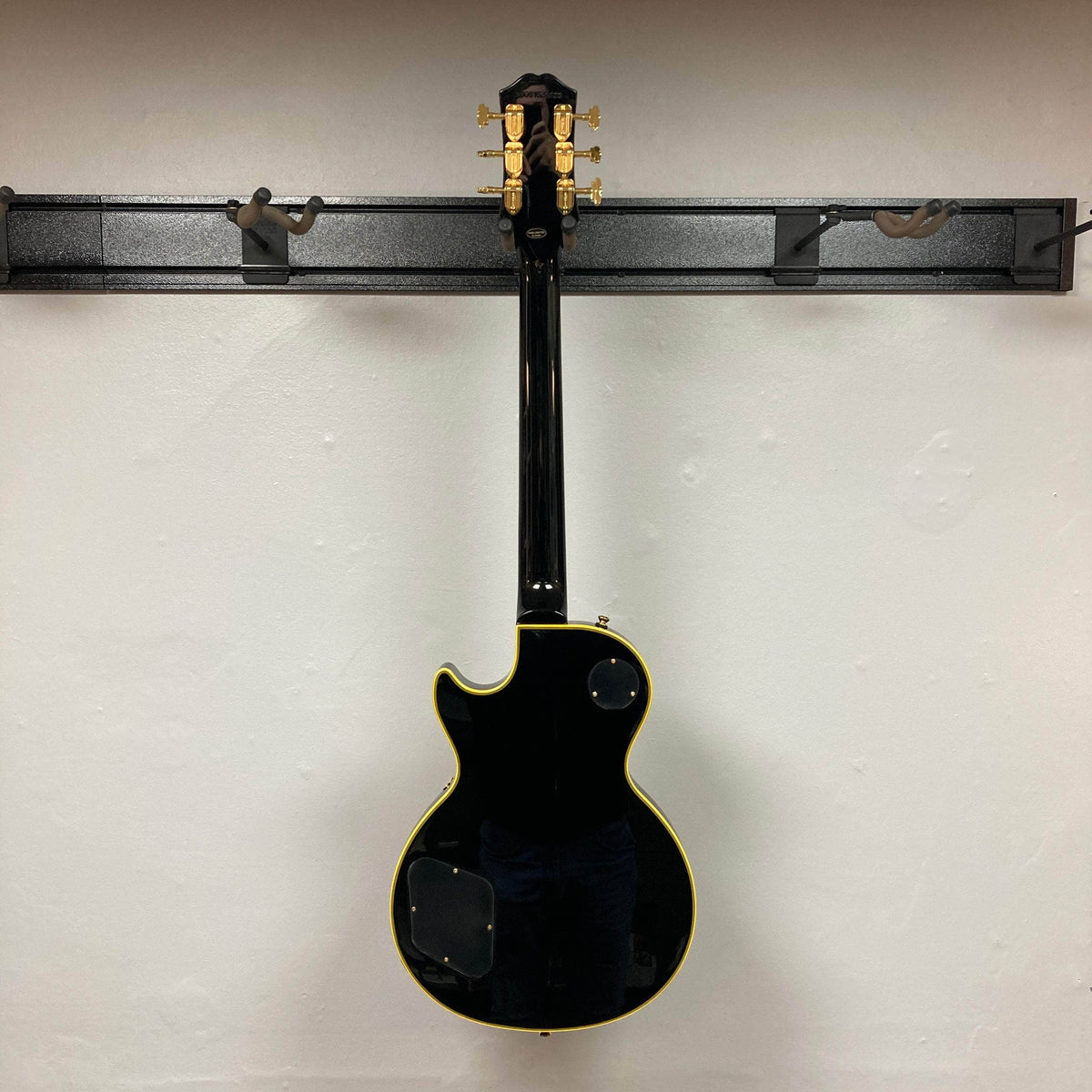 Epiphone Joe Bonamassa 59 Les Paul Custom Bigsby displayed from the rear on a wall-mount rack, showcasing its classic shape and craftsmanship.