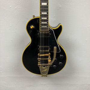 Epiphone Joe Bonamassa '59 Les Paul Custom with Bigsby, featuring gold hardware and dual humbuckers, displayed against a light wall.