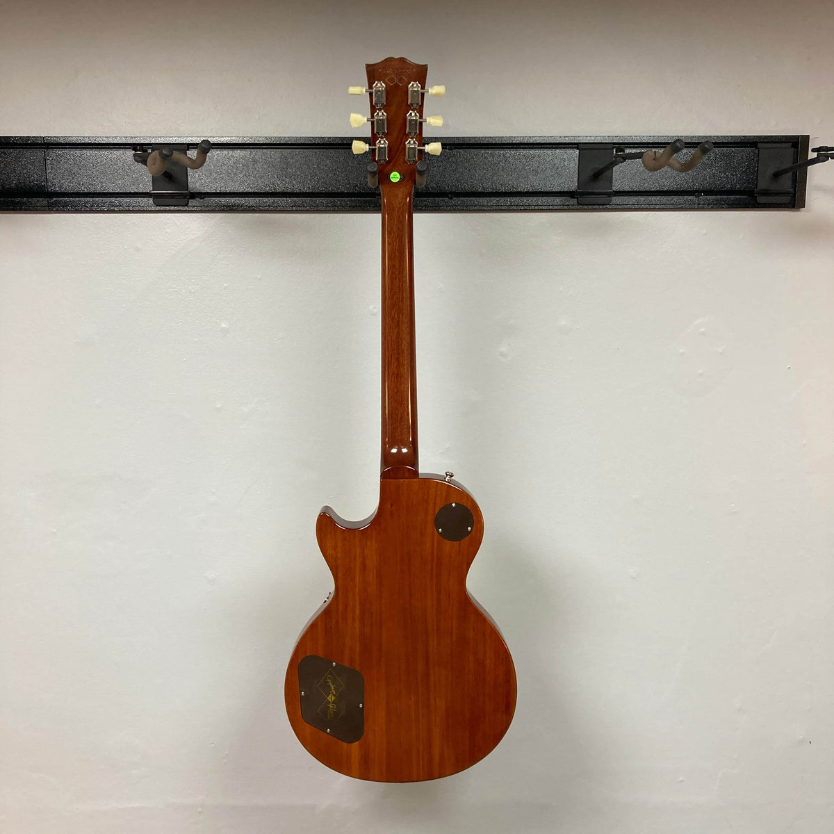 An Epiphone Les Paul 1957 Les Paul Goldtop Reissue Blem w/Case hangs on a wall mount, displayed from the back with visible control cavity covers and tuning pegs.