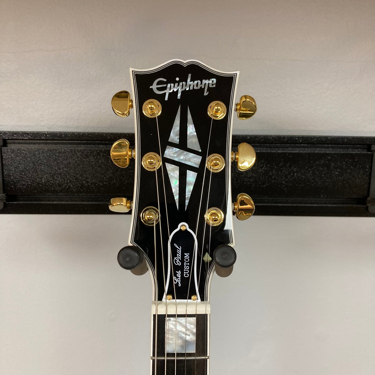 Epiphone Les Paul Custom guitar with gold hardware and mother-of-pearl inlays mounted on a wall.